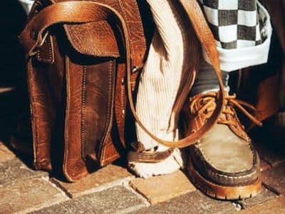 Close-up of leather bag, checkered pants, and vintage shoes on a brick street in Utrecht, Netherlands.